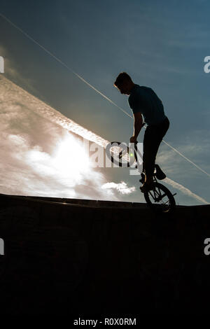 Un rider BMX presso il Plaza, Central Forest park a Stoke on Trent in sella alta e fare acrobazie in silhouette come il sole tramonta Foto Stock