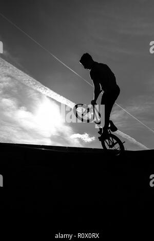 Un rider BMX presso il Plaza, Central Forest park a Stoke on Trent in sella alta e fare acrobazie in silhouette come il sole tramonta Foto Stock