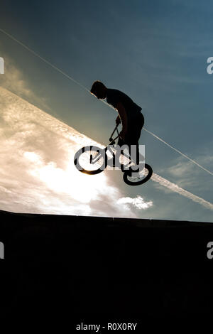 Un rider BMX presso il Plaza, Central Forest park a Stoke on Trent in sella alta e fare acrobazie in silhouette come il sole tramonta Foto Stock