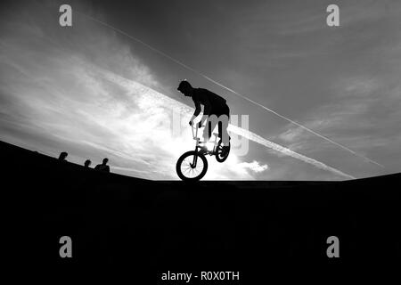 Un rider BMX presso il Plaza, Central Forest park a Stoke on Trent in sella alta e fare acrobazie in silhouette come il sole tramonta Foto Stock