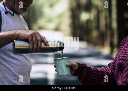 Il vecchio uomo maturo dare ad una donna un caffè caldo in tazza durante il viaggio nel bel mezzo di una foresta per alternative wanderlust vacanza lifestyle fo Foto Stock