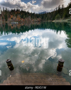 Autunno a colori forest e fronde paesaggi che circondano un idilliaco lago di montagna nelle Alpi della Svizzera su un tardo autunno il giorno con riflessioni nel wate Foto Stock
