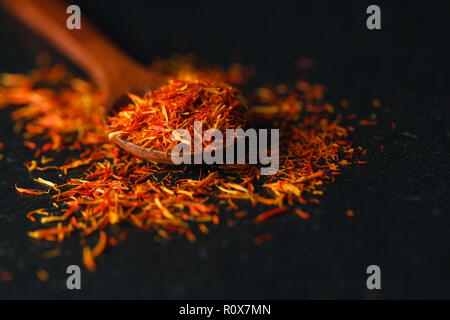 Lo zafferano in un cucchiaio su uno sfondo scuro, il fuoco selettivo, macro shot, profondità di campo Foto Stock