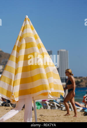 Benidorm, Spagna - 13 Settembre 2011: un giallo e bianco striato brolley spiaggia sulle sabbie di Benidorm, con vacanzieri in passato a piedi Foto Stock