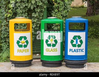 Tre multicolore di cestini per rifiuti con le icone per la comodità di smistamento dei rifiuti posta indesiderata in giardino. Giorno d'estate e di sole Foto Stock