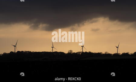 Le turbine eoliche stagliano contro un burrascoso e la cortina di nubi del cielo della sera al tramonto Foto Stock