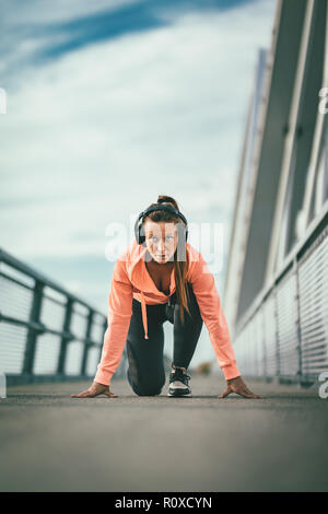 Una giovane donna di sport con le cuffie si prepara per fare jogging al mattino su un ponte sul fiume. Foto Stock