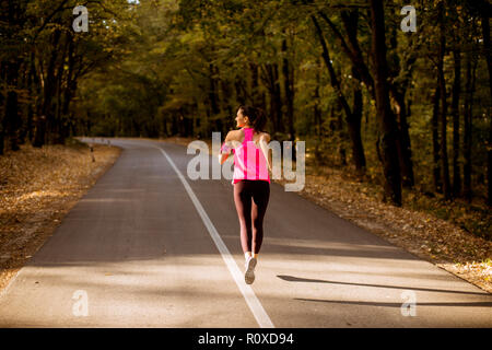 Giovane donna fitness acceso al sentiero forestale in autunno dorato Foto Stock