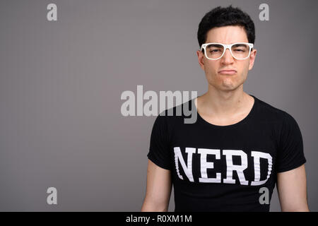 Giovane bello nerd Uomo con occhiali contro uno sfondo grigio Foto Stock