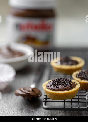 La nutella tortine con cioccolato spruzza su un supporto rack con nutella in background Foto Stock