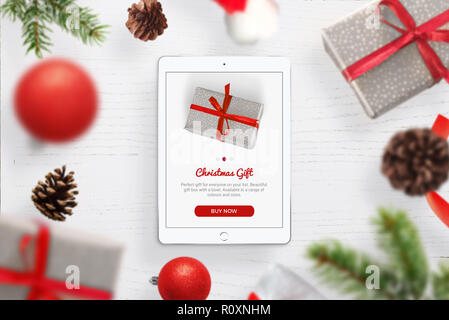 L'acquisto di regali di Natale online. Tablet sul tavolo, circondato da regali di Natale e decorazioni. Foto Stock