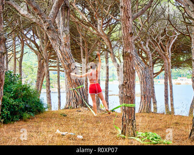 Una giovane donna pratica Slacklining con un nastro teso tra due pini di una foresta mediterranea in Catalogna, Spagna. Foto Stock