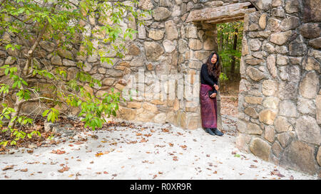 Donna in sarong appoggiata contro la parete in aprire porta in scena a anfiteatro in pietra Foto Stock