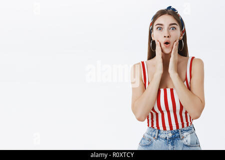 Oh wow che è impressionante. Ritratto di sorpresi e affascinati giovane ed elegante di buona ricerca europea di donna con capelli biondi nessun trucco e striato di piegatura superiore labbra in segno di stupore di toccare le guance in posa mesmerized Foto Stock