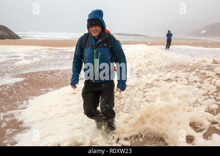 Gli escursionisti in spume o schiuma di mare viene soffiato lungo la spiaggia a Sandwood Bay durante il gale force venti, Sutherland, Scotland, Regno Unito. Foto Stock