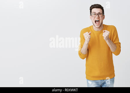 La Pizza è arrivato infine urrà. Ritratto di celebrare la felice eccitato bella giovane maschio in un maglione e bicchieri clenching pugni in trionfo e gioia in piedi in posa di vittoria, lieti e soddisfatti Foto Stock