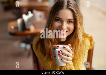 Giovane donna affascinante un caffè mentre è seduto da solo in una caffetteria durante il tempo libero. Ritratto femminile attraente con un simpatico sorriso mentre io appoggio Foto Stock