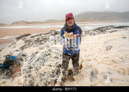 Un escursionista giocando in spume o schiuma di mare sulla spiaggia di Sandwood Bay durante il gale force venti, Sutherland, Scotland, Regno Unito. Foto Stock