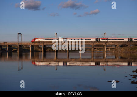 Una vergine treni pendolino di treno sulla linea principale della costa occidentale a Mossband a nord di Carlisle riflessa nelle acque del fiume Esk Foto Stock