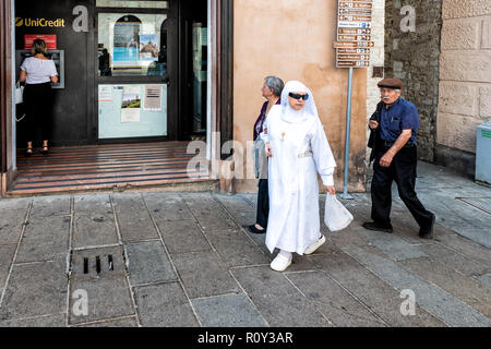 Assisi, Italia - 29 agosto 2018: suora cattolica in abito bianco, abito, occhiali da sole camminando sul marciapiede di strada, strada in antico, vecchio, antque città, t Foto Stock