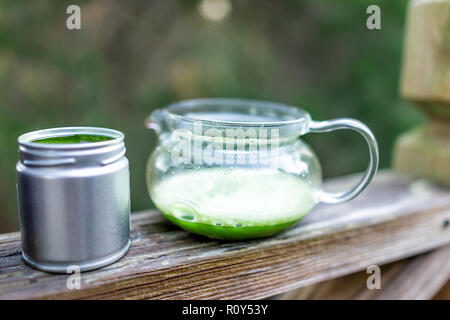 Teiera in vetro sulla ringhiera in legno al di fuori sul ponte del cortile giardino, riempito con vibrante giapponese del tè verde Matcha colore, schiuma in mattinata Foto Stock