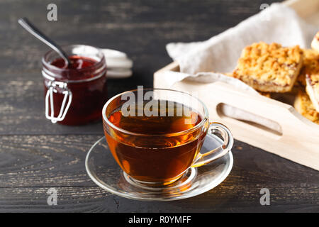 Tazza di tè e il cestello con biscotti serviti per colazione sul tavolo di legno, sfondo scuro Foto Stock