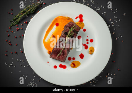 Fette di arrosto di manzo sul piatto bianco decorato su sfondo scuro Foto Stock