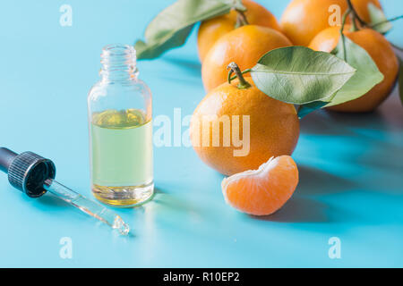 Olio essenziale di arancio mandarino in una bottiglia di vetro pastello su sfondo blu. Dermocosmesi concetto. Foto Stock