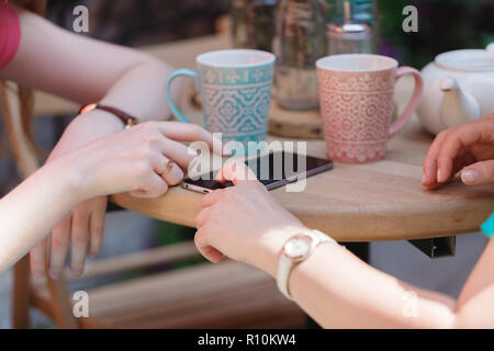 One-to-one di riunione. Due giovani donne seduta a tavola in cafe. Ragazza mostra il suo amico immagine sullo schermo dello smartphone Foto Stock