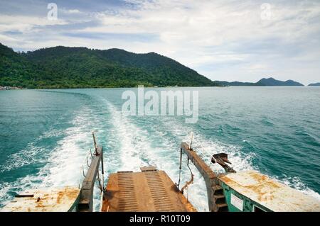 Rampa di traghetto e tracciare sull'acqua di mare tropicale dietro il traghetto, con Koh tropicale Isola Chang sull orizzonte in Thailandia Foto Stock