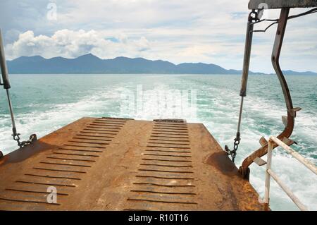 Rampa di traghetto e tracciare sull'acqua di mare tropicale dietro il traghetto, con Koh tropicale Isola Chang sull orizzonte in Thailandia Foto Stock