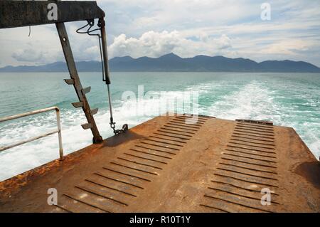 Rampa di traghetto e tracciare sull'acqua di mare tropicale dietro il traghetto, con Koh tropicale Isola Chang sull orizzonte in Thailandia Foto Stock