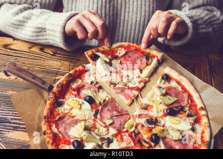 La donna le mani prendere un pezzo di dolce pizza calda con prosciutto, carciofi, olive e pomodori Foto Stock