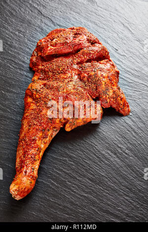 Materie tutta la gamba di Agnello marinato con tutte le spezie e le erbe su una pietra nera vassoio, preparato per essere arrostito, vista verticale da sopra Foto Stock