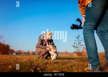 Videografo catturare la donna con il cane nel parco d'autunno. Uomo con steadicam e fotocamera per effettuare riprese. Riprese video Foto Stock