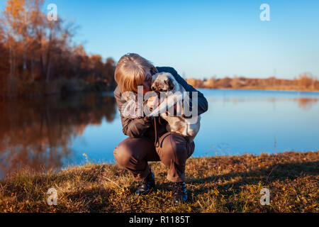 Master pug a piedi un cane in autunno parco dal fiume. Donna Felice costeggiata ed alimentazione di pet. Foto Stock