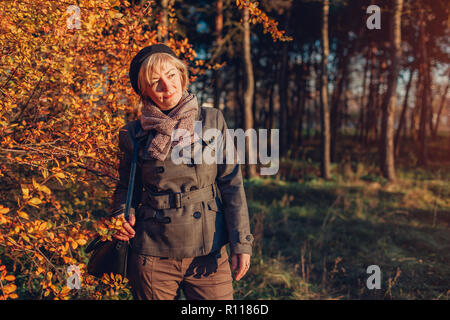 Donna di mezza età a piedi nella foresta di autunno. Senior lady indossando caduta elegante vestito con accessori Foto Stock