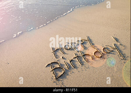 Buon compleanno! Messaggio scritto a mano liscia in sabbia con lente festosa svasatura sulla riva di una spiaggia vuota Foto Stock
