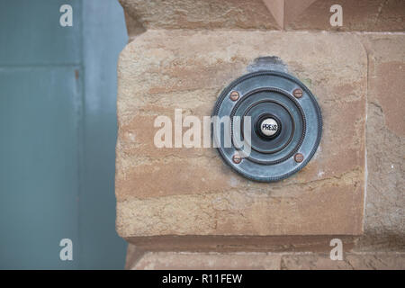 Un vecchio ottone pulsante del campanello su un muro di pietra con una porta Foto Stock