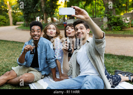 Immagine di felice giovani amici all'aperto nel parco divertendosi in posa bere soda prendere un selfie tramite telefono. Foto Stock
