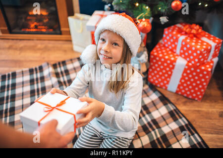 Allegro ragazzina prende con scatola regalo e guarda a adulto che dà lei. Sorride un po'. Ragazza è riconoscente. Si siede su una coperta. Ci sono un altro Foto Stock