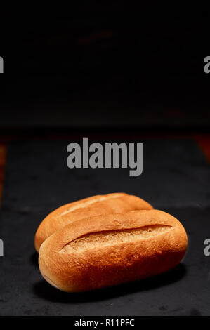 Appena fatto pane normale bun sulla pietra nera tagliere. Molto leggera profondità di campo Foto Stock