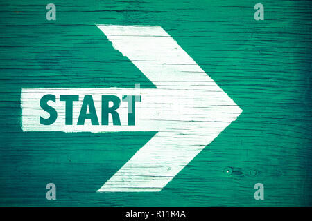 Avviare il testo scritto su bianco freccia direzionale rivolta a destra dipinta su un verde cartello in legno sfondo. Concetto di motivazione per la linea di partenza per autobus Foto Stock