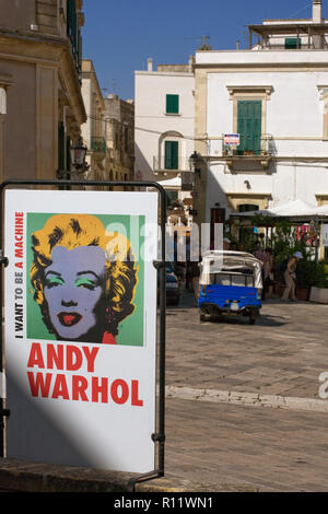 Piazza Alfonso d'Aragona, Otranto, Puglia, Italia: un poster pubblicitari di Andy Warhol mostra 'Voglio essere una macchina" Foto Stock