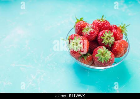 Fresche fragole mature nel recipiente isolato sul morbido sfondo blu. appena raccolto le fragole sul colore smeraldo tabella. Uno stile di vita sano con frutta.spazio copia Foto Stock