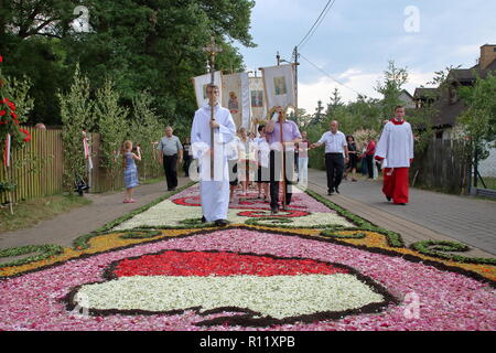I sacerdoti e il popolo durante la processione annuale per celebrare il Corpus Christi, vacanze a piedi con la croce e i religiosi emblemi su tappeti floreali in Spycimierz Foto Stock