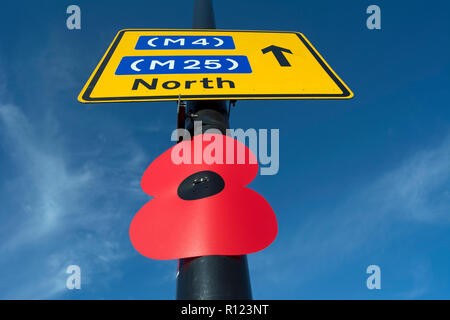 Oversized ricordo il papavero attaccato ad un lampione sotto un cartello stradale per la m4 e la m25 in direzione nord, a Hounslow, Middlesex, Inghilterra Foto Stock