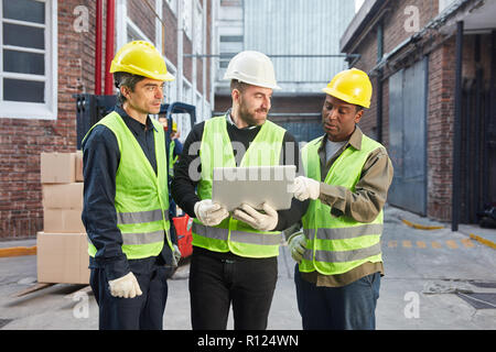 Tre dei lavoratori che utilizzano notebook come una squadra logistica sono la pianificazione di una consegna nel lavoro di squadra Foto Stock