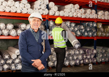Senior sorridente come un apritoio con esperienza nel magazzino di tappeti Foto Stock