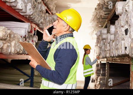 Lavoratori anziani in deposito nel magazzino di tappeti sta parlando al telefono Foto Stock